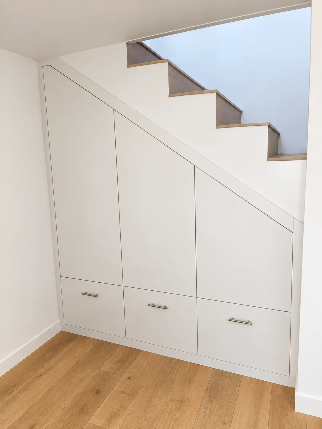 Placards blancs sur mesure intégrés sous un escalier en bois